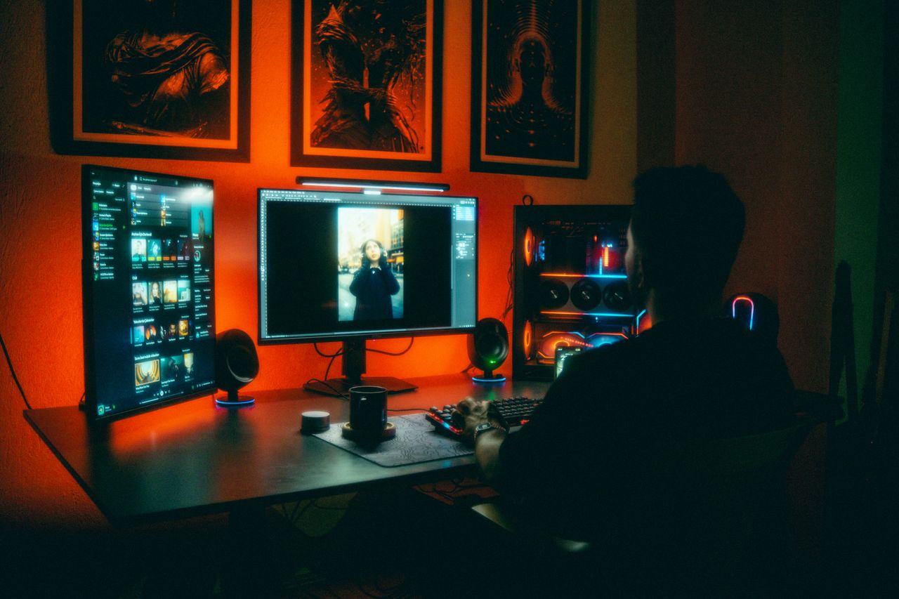 our-experience A person editing photos at night in a neon-lit home office with dual screens.